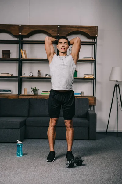 Zwei-Rassen-Mann steht in Sportbekleidung und trainiert im Wohnzimmer — Stockfoto