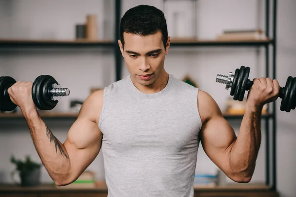 Guapo y fuerte hombre bi-racial haciendo ejercicio con pesas en la sala de estar - foto de stock