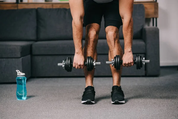 Обрезанный вид сильного мускулистого человека тренировки с гантелями в домашнем тренажерном зале — стоковое фото