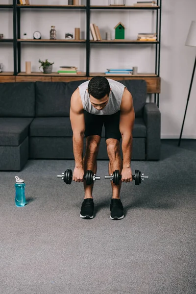 Strong mixed race man training with dumbbells in living room — Stock Photo