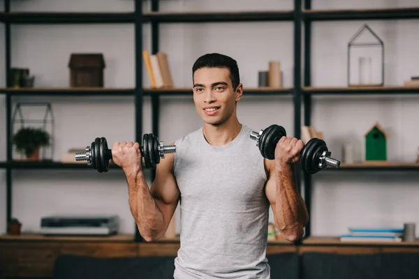 Sorrindo misto corrida homem treino com halteres na sala de estar — Fotografia de Stock