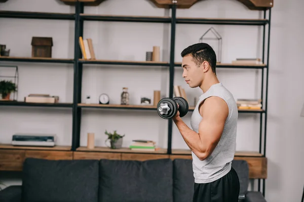 Bonito misto raça desportista fazendo exercício com halteres na sala de estar — Fotografia de Stock