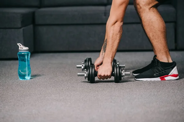 Ausgeschnittene Ansicht eines Sportlers, der Hanteln im Wohnzimmer auf den Boden legt — Stockfoto
