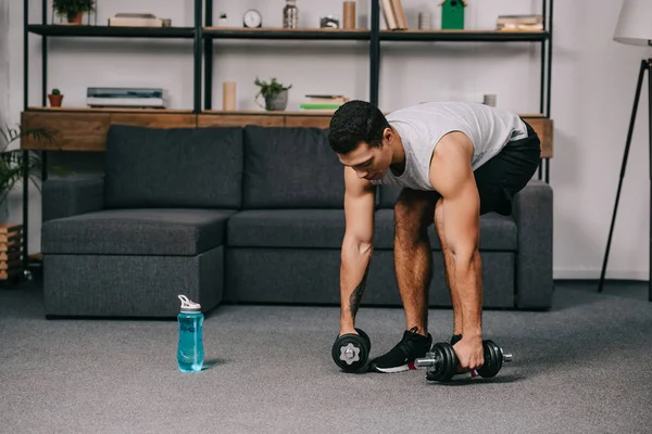 Mixed race sportsman taking dumbbells from floor in living room — Stock Photo