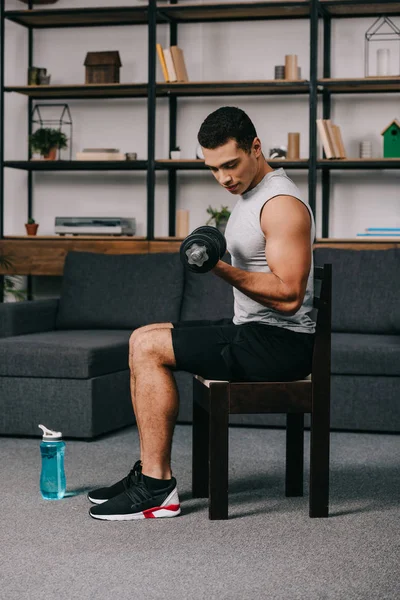 Strong mixed race sportsman training with heavy dumbbell on chair — Stock Photo