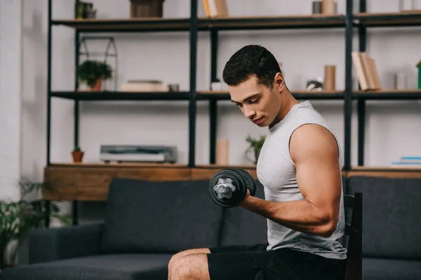 Powerful mixed race sportsman training with heavy dumbbell on chair — Stock Photo