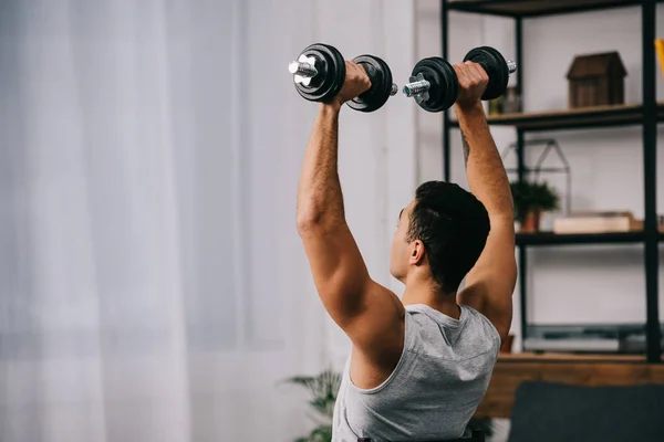 Musculoso amixed raza hombre holding pesado dumbbells sobre cabeza - foto de stock