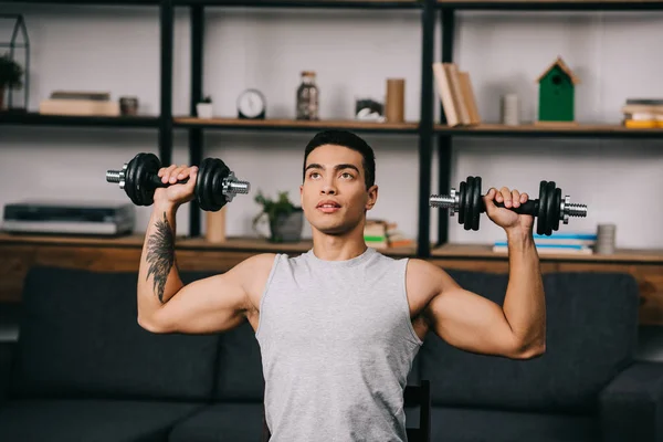 Handsome mixed race athlete exercising with dumbbells in living room — Stock Photo