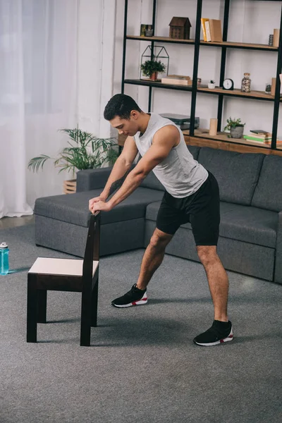 Mixed race athlete using chair for exercise in living room — Stock Photo