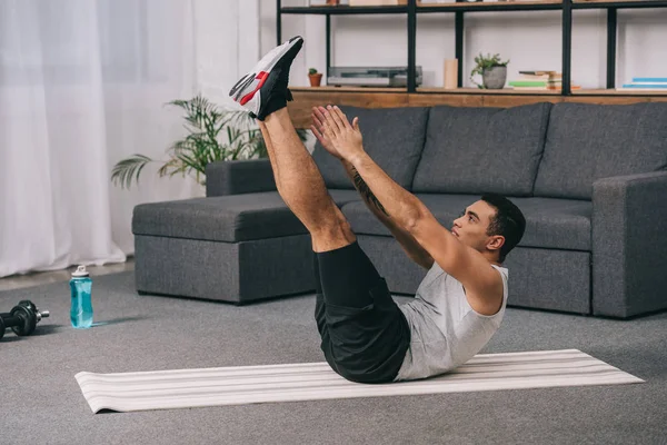 Hombre de raza mixta fuerte haciendo ejercicio en la estera de fitness en la sala de estar - foto de stock