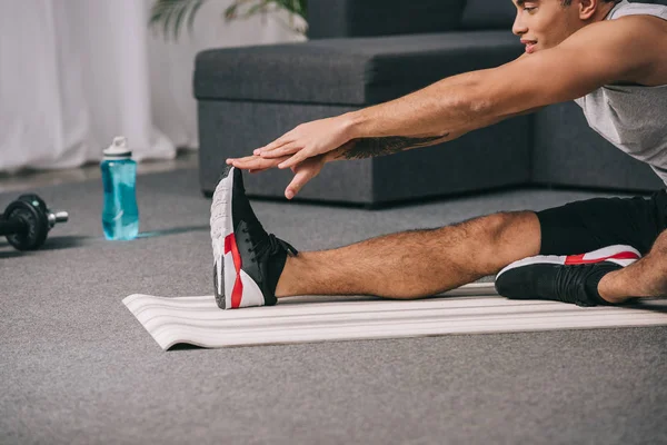 Cropped view of mixed race man stretching on fitness mat in living room — Stock Photo