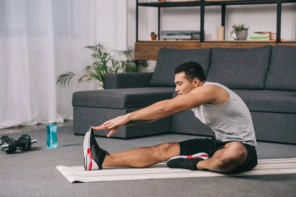 Hombre de raza mixta haciendo ejercicio de estiramiento en la estera de fitness en la sala de estar - foto de stock