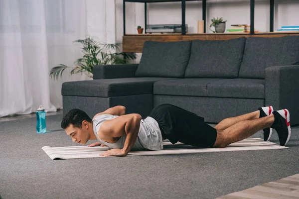 Bi-racial hombre haciendo flexiones en fitness mat en apartamento - foto de stock