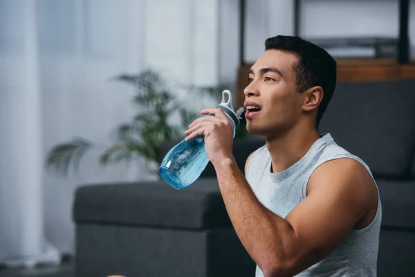 Весёлый двурасовый мужчина пьёт воду из спортивной бутылки — стоковое фото