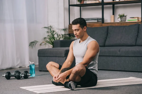Handsome bi-racial man sitting on fitness mat with closed eyes — Stock Photo