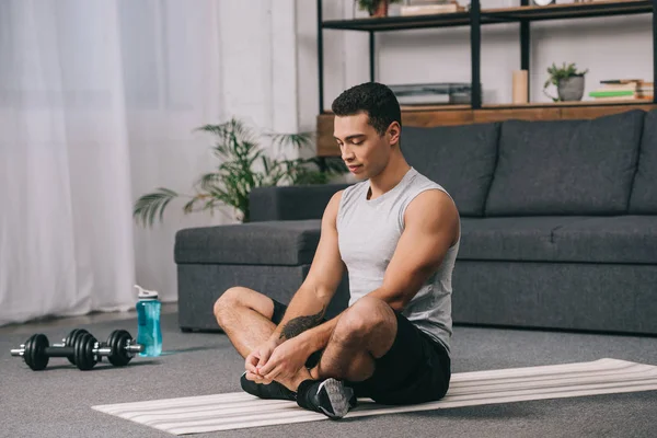 Bel homme bi-racial assis sur un tapis de fitness avec les yeux fermés — Photo de stock