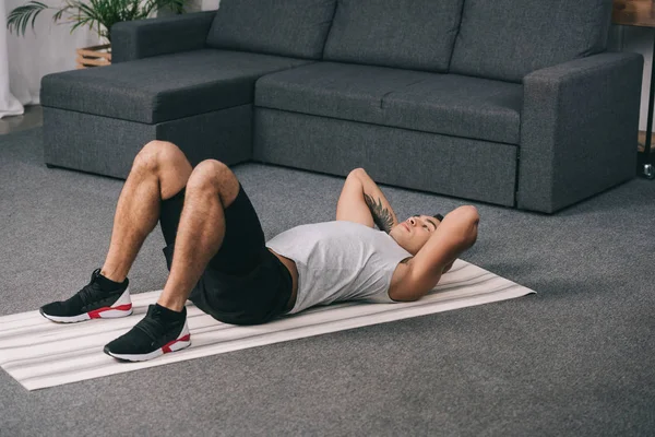 Tattooed bi-racial man lying on fitness mat and doing exercise — Stock Photo