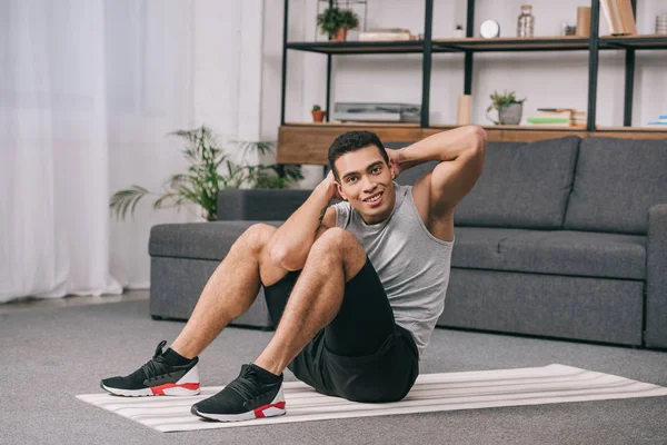 Guapo bi-racial hombre sentado en yfitness mat y haciendo ejercicio - foto de stock