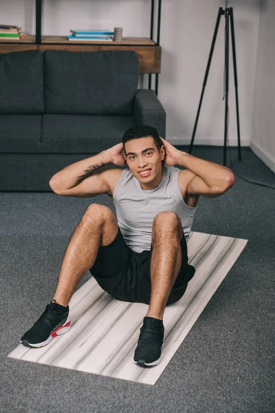 Happy bi-racial man sitting on fitness mat and doing exercise — Stock Photo