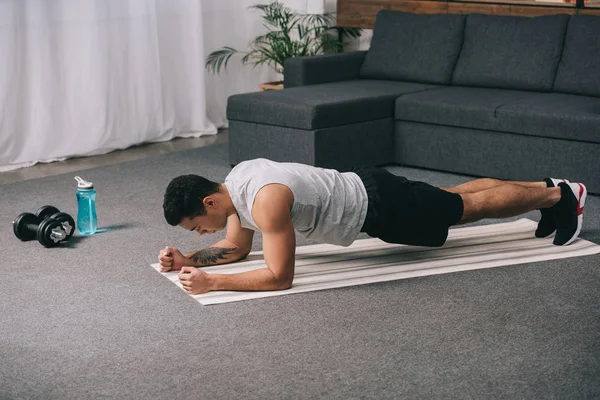 Atleta bi-razziale che fa esercizio plancia sul tappeto fitness — Foto stock