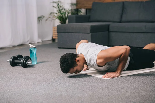 Сильный бирасовый спортсмен делает упражнения на тренажерном коврике в квартире — стоковое фото
