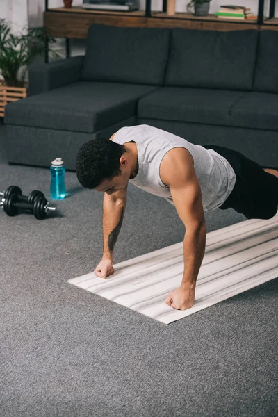 Deportista bi-racial haciendo flexiones en ropa deportiva en la alfombra de fitness - foto de stock