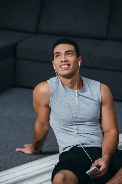 Handsome bi-racial man holding smartphone and listening music in earphones — Stock Photo