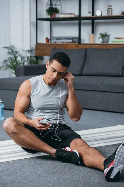 Hombre bi-racial sosteniendo teléfono inteligente y escuchar música en los auriculares con los ojos cerrados - foto de stock