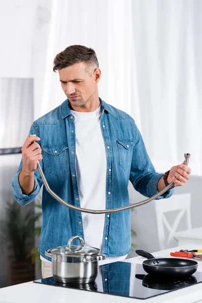 Homem confuso segurando mangueira de metal enquanto estava na cozinha — Fotografia de Stock