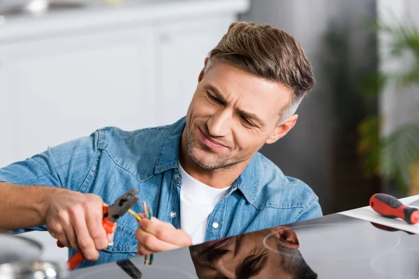 Bel homme réparant cuisinière électrique à la cuisine avec pince — Photo de stock