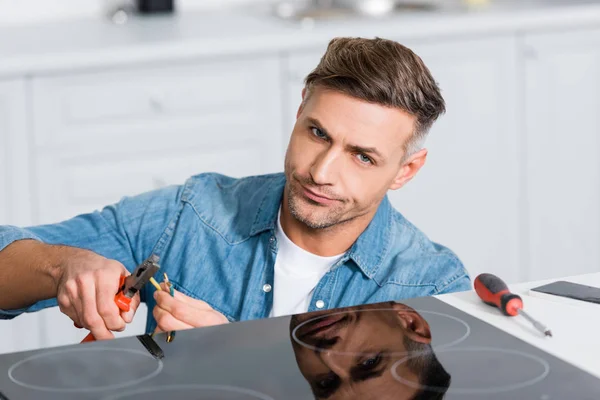 Confused man repairing wires of kitchen stove — Stock Photo