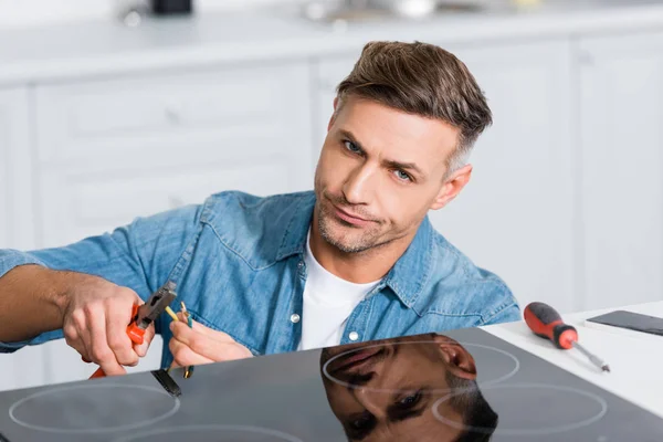 Verwirrter Mann repariert Kabel von Küchenherd — Stockfoto