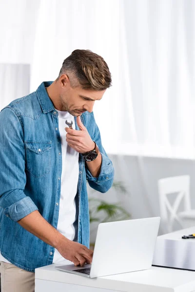 Thoughtful man holding repair tool and using laptop — Stock Photo