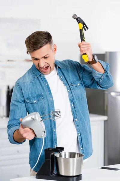 Agresivo hombre adulto gritando mientras sostiene mezclador y martillo - foto de stock