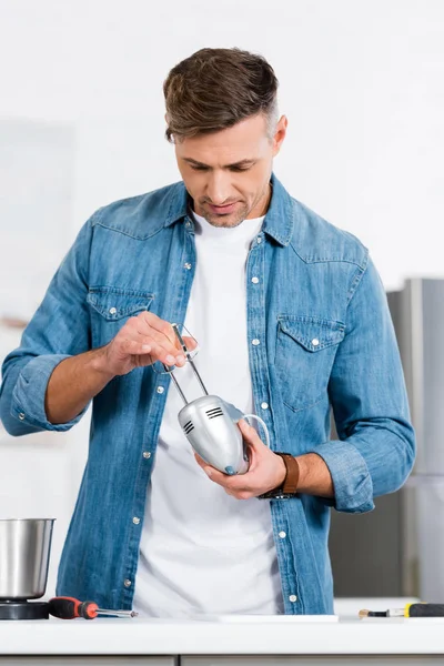 Homem bonito em camisa jeans reparando misturador de cozinha — Fotografia de Stock