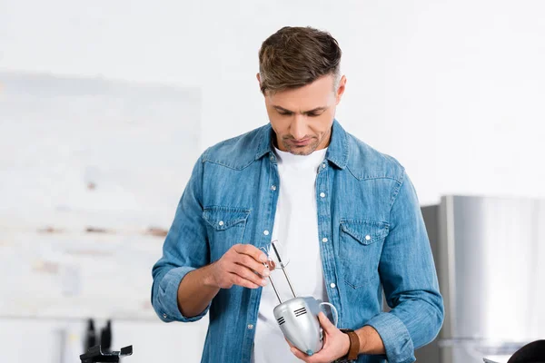 Handsome man holding kitchen mixer in hands and looking at it — Stock Photo
