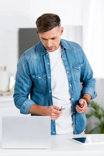 Handsome man holding repair tools and looking at laptop — Stock Photo