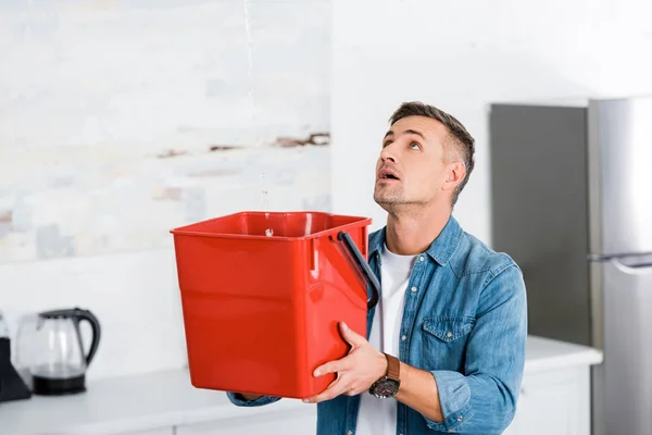 Homem bonito segurando balde de plástico e olhando para o teto — Fotografia de Stock