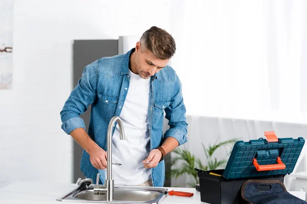 Schöner erwachsener Mann repariert Wasserhahn bei Küche — Stockfoto