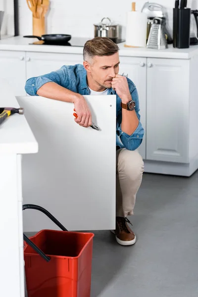 Nachdenklicher Mann hält Zange in der Hand neben rotem Eimer — Stockfoto