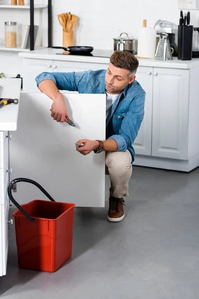 Confused man repairing kitchen sink — Stock Photo