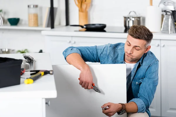 Trauriger Mann hält Zange in der Hand, während er Küchenspüle repariert — Stockfoto