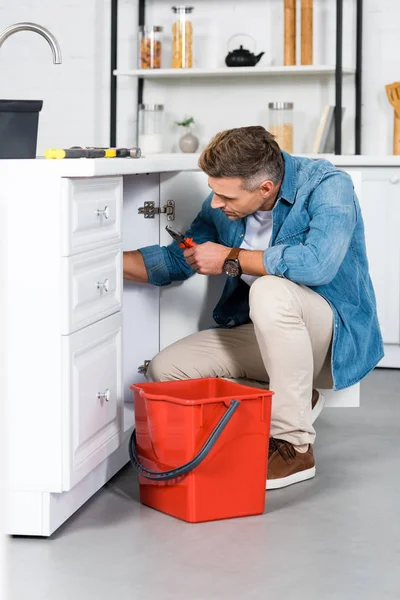 Homem adulto bonito reparando pia da cozinha — Fotografia de Stock