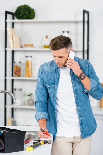 Adult man talking on smartphone white holding pliers — Stock Photo