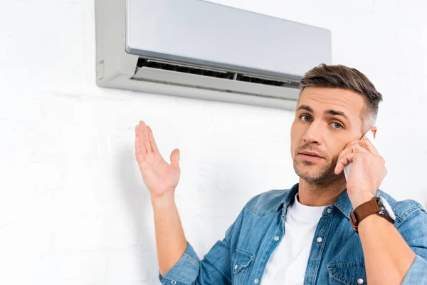 Homem bonito falando no smartphone enquanto está perto do ar condicionado — Fotografia de Stock