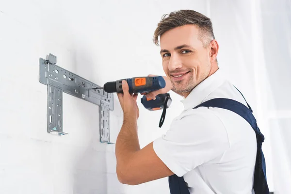 Sonriente reparador adulto instalando soporte para aire acondicionado con taladro - foto de stock