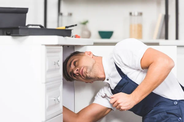 Erwachsener Reparateur hält Schraubenschlüssel bei Kontrolle von Rohren in Küche — Stockfoto