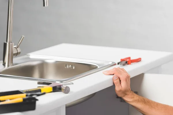 Vista recortada de la mano masculina apoyada en el mostrador de la cocina con grifo cerca de herramientas - foto de stock