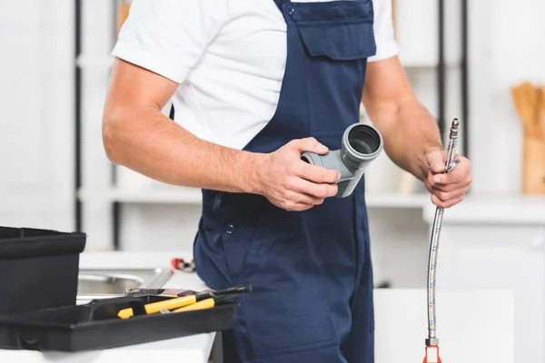 Cropped view of repairman holding pipes for repairing kitchen faucet — Stock Photo