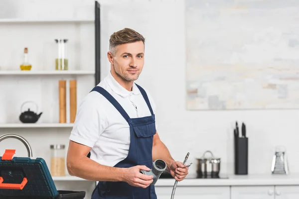 Erwachsener Reparateur hält Rohre für die Reparatur von Küchenarmaturen und schaut in die Kamera — Stockfoto